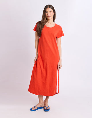Woman wearing a bright orange linen maxi dress and blue flip flops.