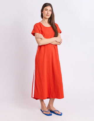 Woman wearing a bright red linen midi dress and blue flip flops standing against a white background.