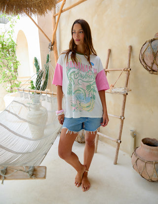 Woman wearing a white and pink Bahamas graphic t-shirt and denim shorts in a tropical setting.