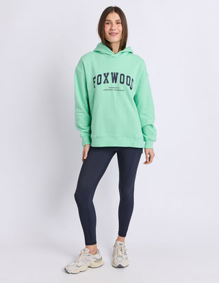 Woman wearing a mint green Foxwood oversized hoodie and dark navy leggings.