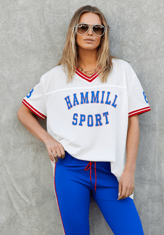 Woman wearing a white Hammill Sport mesh jersey and blue athletic pants.
