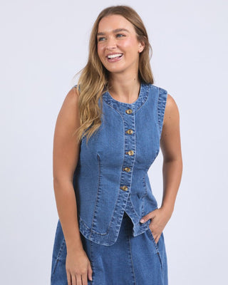 Woman wearing a sleeveless blue denim button-up vest and matching denim skirt.