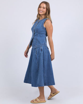 Woman wearing a blue denim vest and matching midi skirt with straw sandals.