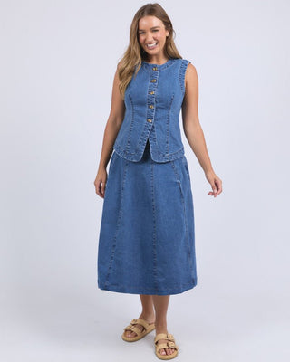Woman wearing a blue denim sleeveless button-up vest and matching midi skirt with sandals.