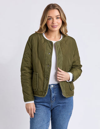 Woman wearing an olive green quilted jacket over a white top and blue jeans.