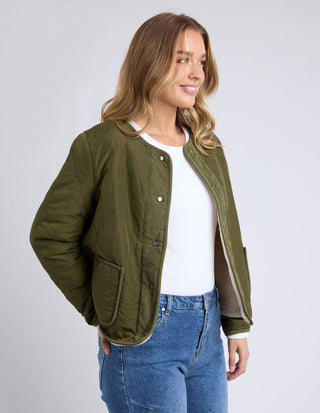 Woman wearing an olive green quilted lightweight jacket over a white top and blue jeans.