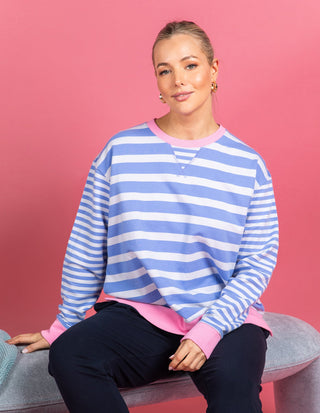 Woman wearing a blue and white striped sweatshirt with pink trim and navy pants.