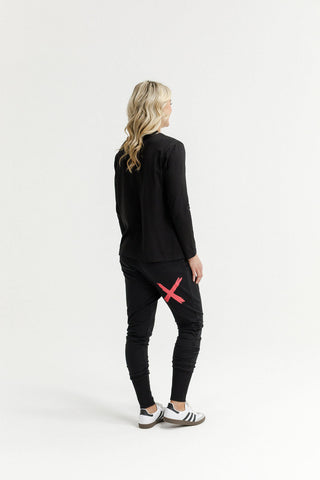 Rear view of a woman wearing a black long sleeve top and black joggers with a red X detail.