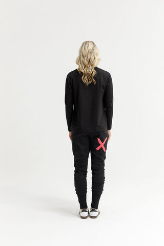 Rear view of a woman wearing a black long-sleeve top and black joggers with a red X design.