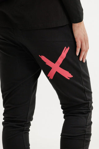 Close-up of black joggers featuring a large red cross graphic on the thigh.