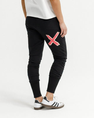 Woman wearing black leisure wear joggers with a pink X graphic detail and white sneakers.