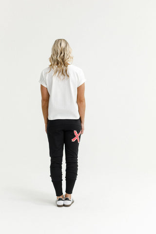 Woman from behind wearing a white t-shirt and black joggers with a red X detail.