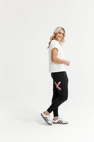 Woman wearing a white t-shirt and black joggers with red graphic detail and white sneakers.