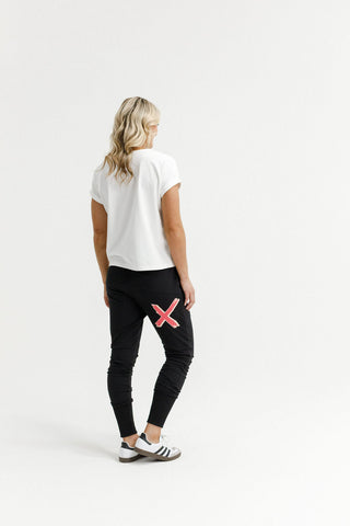 Woman wearing a white t-shirt and black joggers with a pink X detail on the back.
