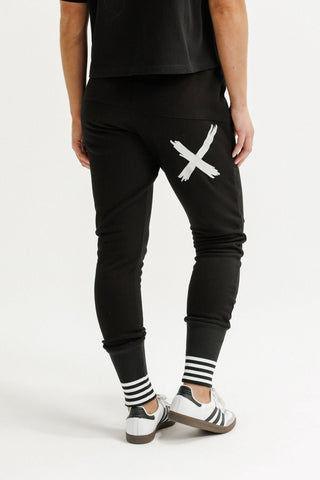 Man wearing black joggers with a large white X graphic and striped cuff details.