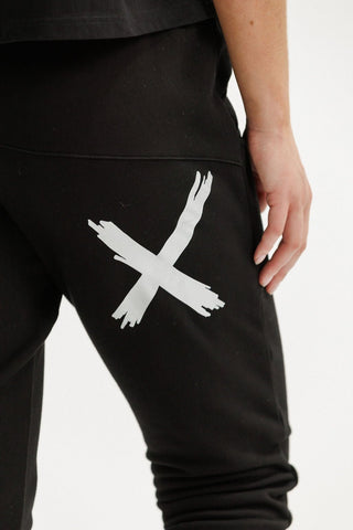 Black leisure wear joggers featuring a large white brushstroke X graphic on the thigh.