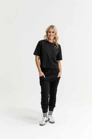 Woman smiling in black oversized t-shirt and matching black joggers with striped cuffs.