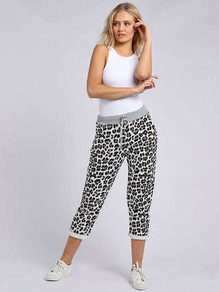 Woman wearing white tank top and leopard print joggers with grey waistband.