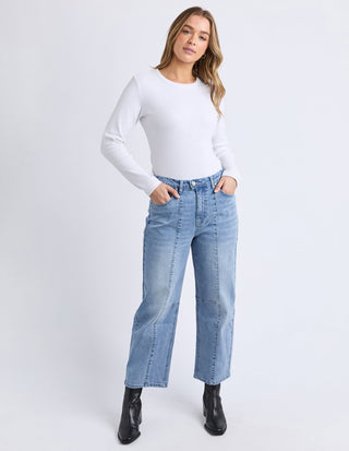 Woman wearing a white long-sleeve t-shirt, light blue wide-leg jeans, and black ankle boots.
