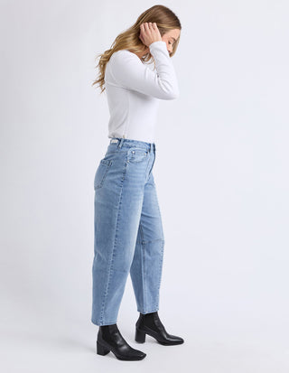Woman wearing a white long sleeve top, light blue jeans, and black ankle boots.