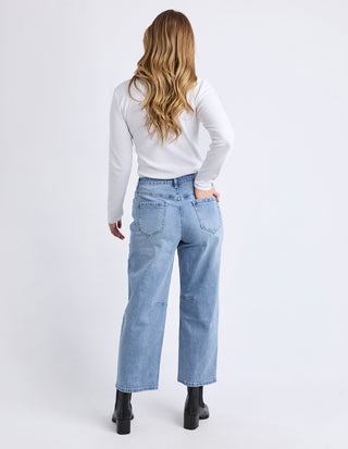Woman from behind wearing a white long-sleeve top, light blue wide-leg jeans, and black boots.