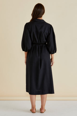 Back view of a woman wearing a black midi shirt dress with puff sleeves and a waist tie.
