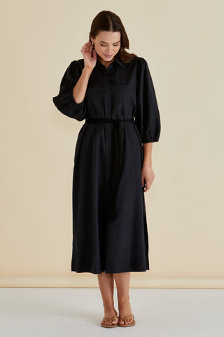 Woman wearing a long-sleeved black shirt dress with a matching waist tie and tan sandals.