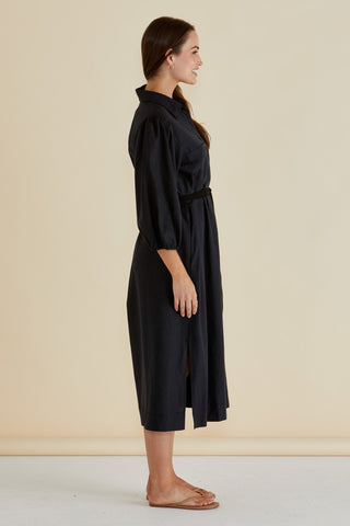 Woman in a black midi dress with puff sleeves and a belted waist, side view.