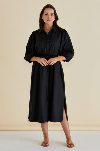 Woman wearing a black midi shirt dress with balloon sleeves and a waist tie.