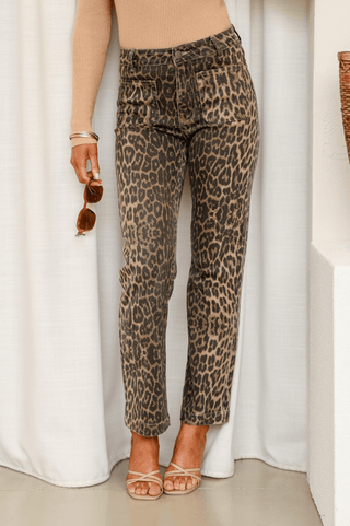 Woman wearing leopard print slim-fit pants and a beige long-sleeve top with strappy sandals.