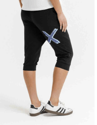 Woman wearing black cropped leisure pants with a blue X graphic and white sneakers