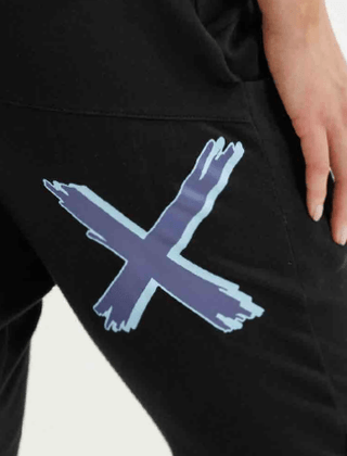 Close-up of black joggers featuring a blue brushstroke X graphic on the leg.