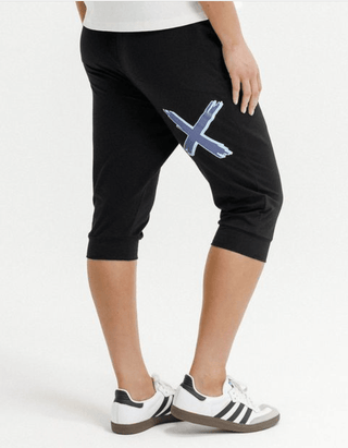 Woman wearing black cropped capri leggings with a blue graphic X design and white sneakers.