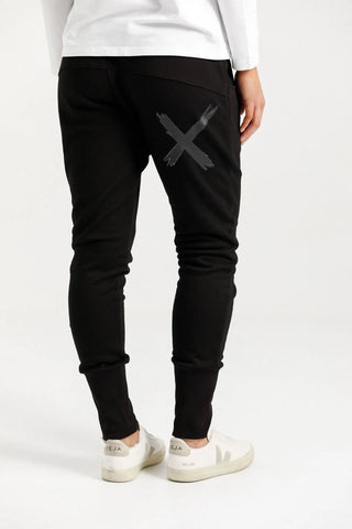 Woman wearing black slim-fit joggers with a grey cross graphic and white sneakers