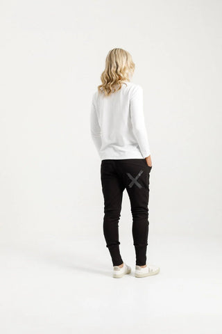 Back view of a woman wearing a white long sleeve top and black joggers with a graphic print.