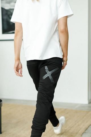 Woman wearing a white t-shirt and black joggers with a grey X graphic on the leg.