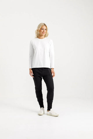 Woman wearing a white long-sleeve top and black joggers with white sneakers.