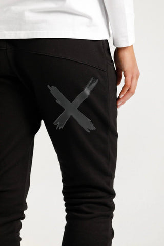 Close-up of black joggers featuring a large grey cross graphic on the thigh