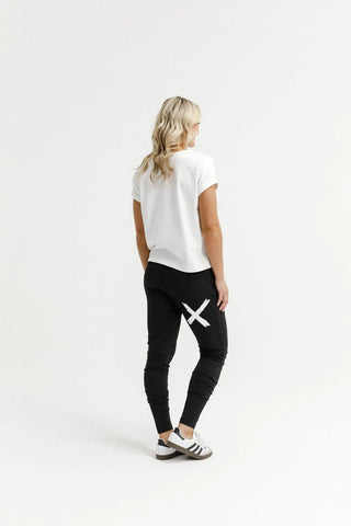 Woman in white t-shirt and black joggers with white graphic detail standing against white background