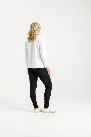 Rear view of a woman wearing a white long-sleeved top and black joggers with white sneakers.