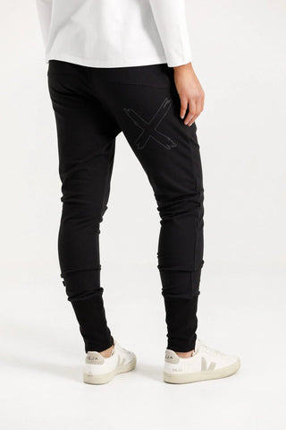 Woman wearing black joggers with a grey X detail and white Veja sneakers.