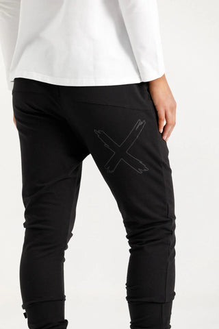 Woman wearing black leisure joggers with a tonal X graphic on the thigh.