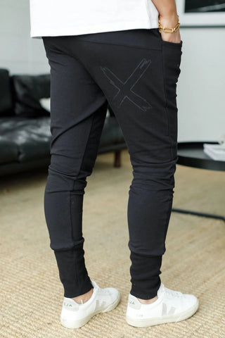Person wearing black tapered joggers with a graphic X design and white sneakers