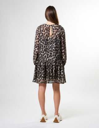 Rear view of a woman wearing a long-sleeved leopard print mini dress and white sneakers.