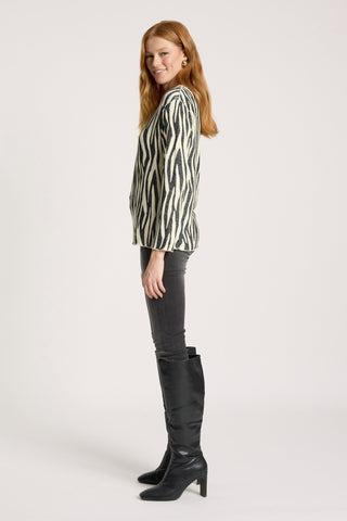 Woman wearing a zebra print long sleeve top, grey skinny pants, and black knee-high boots.