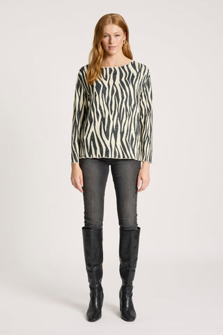 Woman wearing a zebra print long sleeve top, grey skinny jeans, and black knee-high boots.
