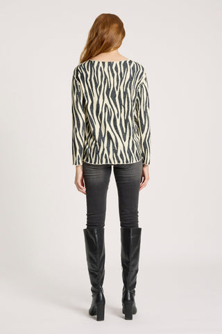 Woman wearing a black and cream zebra print long sleeve top with black skinny jeans and boots.