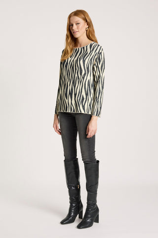 Woman wearing a zebra print top, grey skinny jeans, and black knee-high boots.