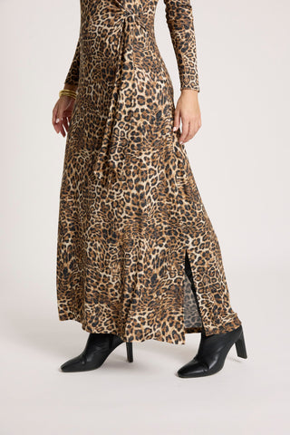 Woman wearing a long-sleeved leopard print maxi dress with a side slit and black ankle boots.