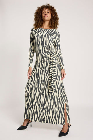 Woman wearing a long-sleeved zebra print maxi dress with a waist tie and side slit.